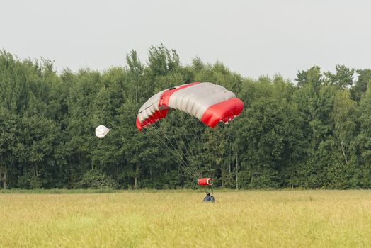 A just landed parachutist with a mattress-shaped parachute in a field
