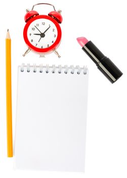 Open copybook with lipstick and alarm clock on isolated white background