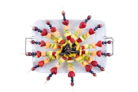 Buffet arrangement of healthy fruit shish kebabs made with diced tropical and exotic summer fruit on a serving tray isolated on white, overhead view