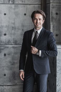 Portrait of smiling businessman in suit over concrete wall background