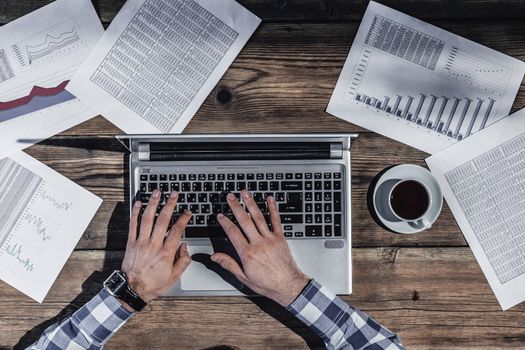 Businessman working on laptop with financial documents, top view