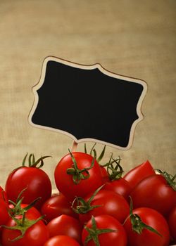 Red ripe fresh small cherry tomatoes with black wooden chalkboard price sign tag close up over jute burlap canvas background