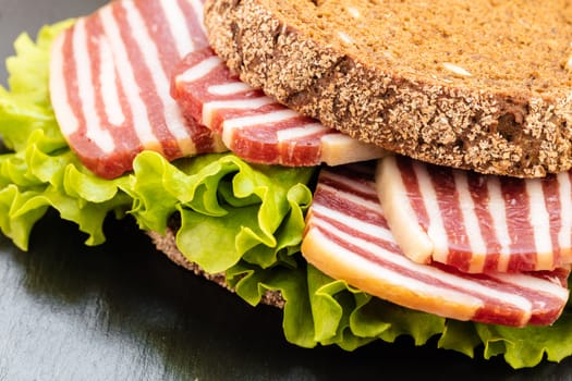 sandwich with sausage and lettuce on a dark background