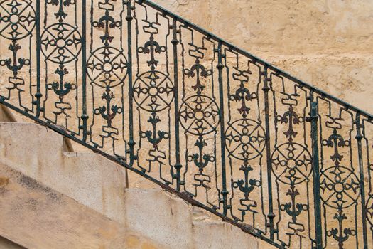 Part of the stairs from a side, with visible rhythm of the steps and iron handrail with motive of compass and anchor. Stone wall in the background. Island Malta