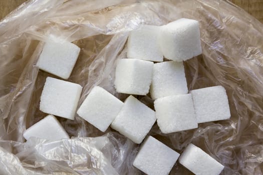 White sugar pieces in a plastic bag on a wooden background.