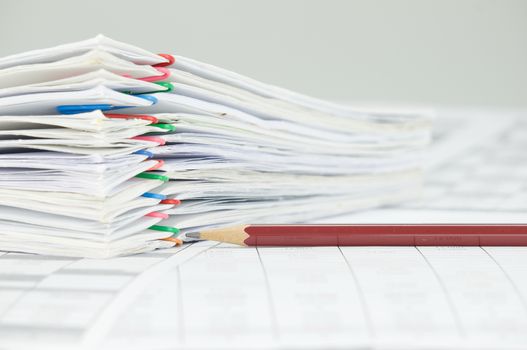 Brown pencil and overload of paperwork with colorful paperclip on finance account place on white background.