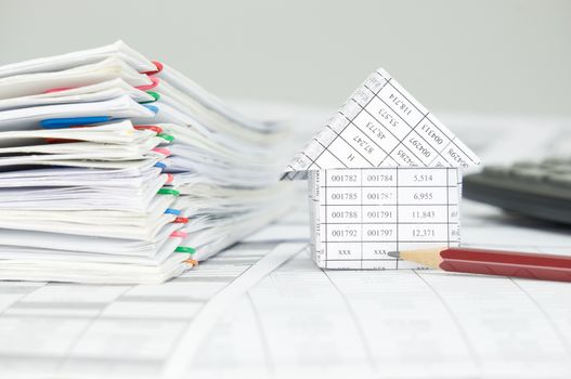 House with brown pencil and overload of paperwork with colorful paperclip on finance account have blur calculator as background.