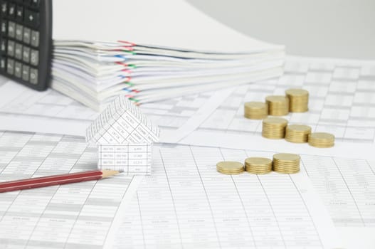 House with brown pencil and step pile of gold coins on finance account have blur calculator place vertical and overload of paperwork with colorful paperclip as background.