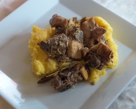 in the picture typical italian food ,roasted goat and Polenta on white dish at restaurant,view from above.