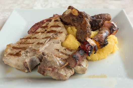 Typical italian grilled meat mix and Polenta on a plate at restaurant,close-up view.