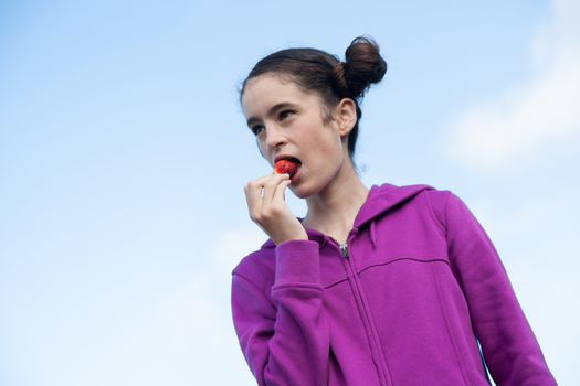 Young woman pops strawberry into mouth while picking in season strwaberries