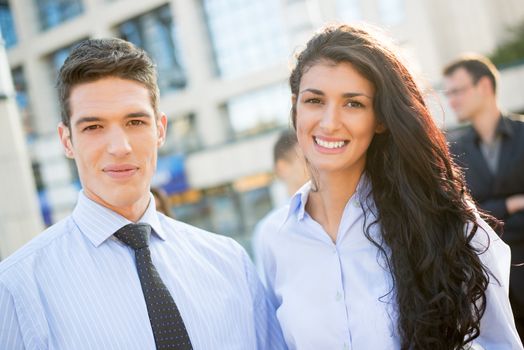 Young and handsome businessman and businesswoman standing in front of the company, smiling looking at camera.