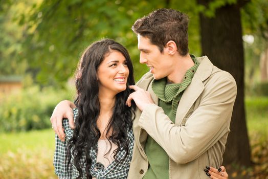 Portrait of a young heterosexual couple walking on the park, embraced, looking at each other.