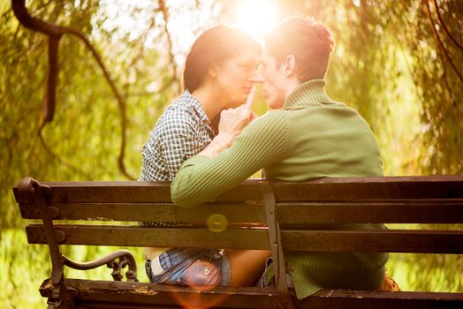 Young couple in love sitting on a park bench photographed from the rear, illuminated background sunlight, passionate look at each other in the moment before the kiss.