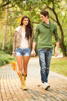Young pretty girl with long legs in shorts and boots holding hands with her handsome boyfriend, walking trails in the park.