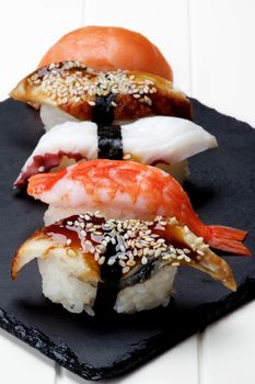 Various Sashimi Sushi with Smoked Eel, Shrimp, Octopus and Salmon In a Row on Stone Plate closeup on White Plank background. Focus on Foreground