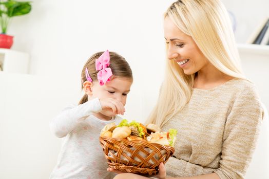 A beautiful young mother gives a wicker basket with fresh pastries her daughter by offering her a variety of delicious baked goods.