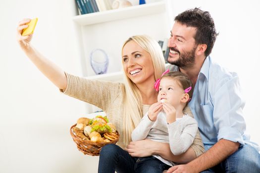 Young beautiful woman photographed with a mobile phone herself, her husband and their beautiful daughter with a wicker basket filled with pastry products.