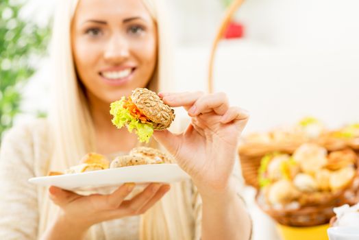 Young beautiful woman with face out of focus keeps at arm's pastry offering the viewer snack while in the background see wicker basket with a bunch of baked treats.