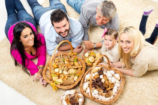 Happy family lying on a carpet in the living room around woven baskets filled with baked goods, looking up with a smile at the camera.