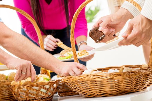 Close-up woven baskets full of baked goods to which a bunch of hands reaching out to take the delicious pastry.