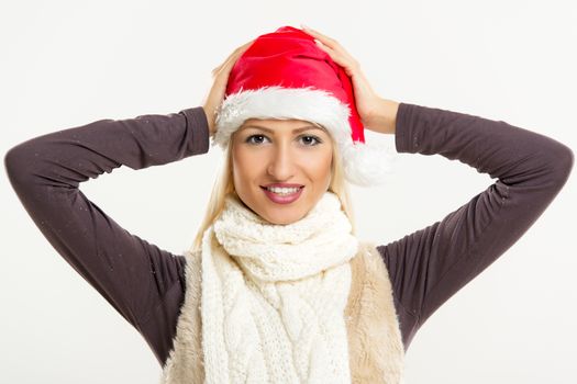 A young pretty blonde girl with a Santa's cap smiling looking at the camera while her hands puts a cap on her head.