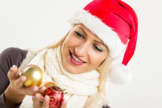 Cute blonde girl with Santa Claus hat and a warm scarf around her neck, holding a decorative globe with a smile on her face looking at them.