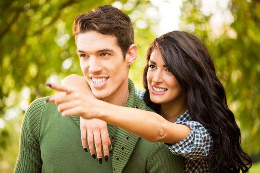 Young heterosexual couple in the park are embraced, while the girl shows a finger-pointing at something.