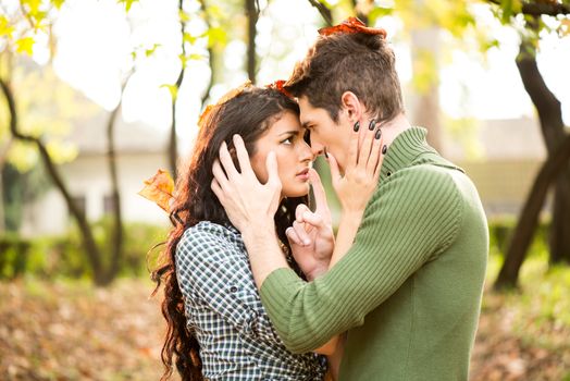 Young heterosexual couple in love in park in the autumn landscape, passionately watch faces turned toward each other, and on their heads were standing fallen autumn leaves.