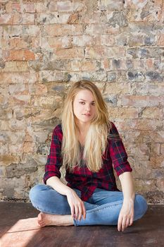 Front view of attractive white girl sitting on wooden floor against concrete wall