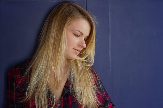 Portrait of a young beautiful girl with closed eyes, a beautiful smile. Posing on a background of an blue wall.