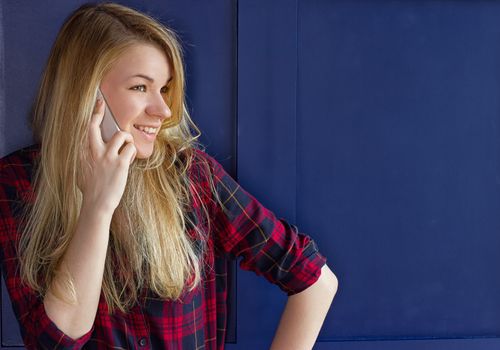 Pretty Woman Calling Someone Through Mobile Phone While Smiling at the Camera Against Blue Wall Background
