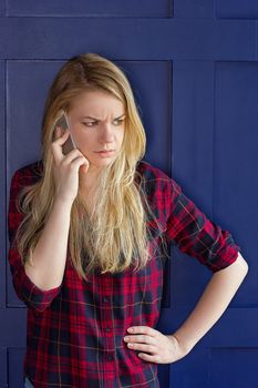 Pretty Woman Calling Someone Through Mobile Phone While Smiling at the Camera Against Blue Wall Background