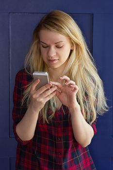 Cute Girl playing with her Phone on a blue Wall