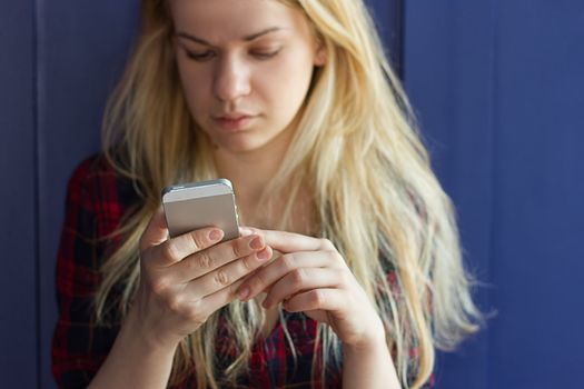 Cute Girl playing with her Phone on a blue Wall