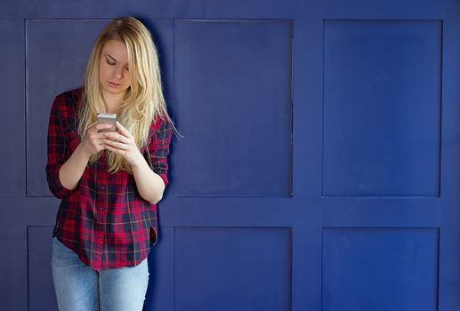 Cute Girl playing with her Phone on a blue Wall