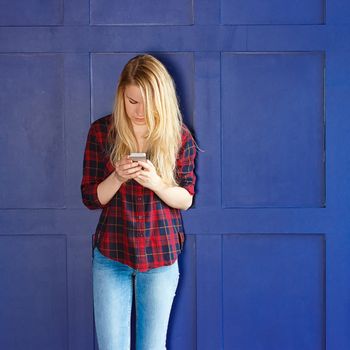 Pretty Woman Calling Someone Through Mobile Phone While Smiling at the Camera Against Blue Wall Background