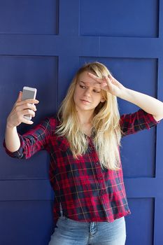 image of beautiful blond young ladr making selfie at blue concrete wall