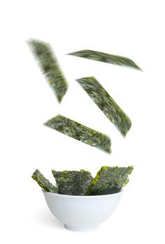 Seaweed slices falling into a bowl over a white background, a superfood that is high in vitamin c, iron and promotes healthy bacteria in the gut 