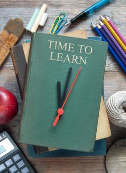 Clock hands pointing towards time to learn on book with educational items around it