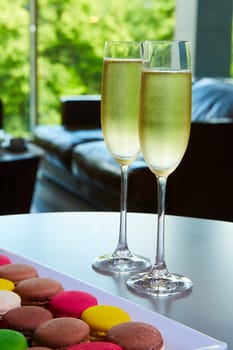 Two glasses of sparkling wine or champagne on a table with small colorful macaroons