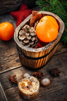 Wooden bucket with tangerines and pine cone and a burning Christmas candle