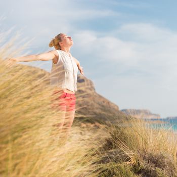 Relaxed woman, arms rised, enjoying sun, freedom and life an a beautiful beach. Young lady feeling free, relaxed and happy. Concept of vacations, freedom, happiness, enjoyment and well being.