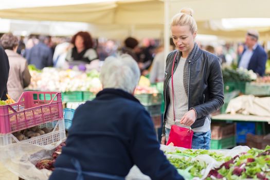 Woman buying fruits and vegetables at local food market. Market stall with variety of organic vegetable.