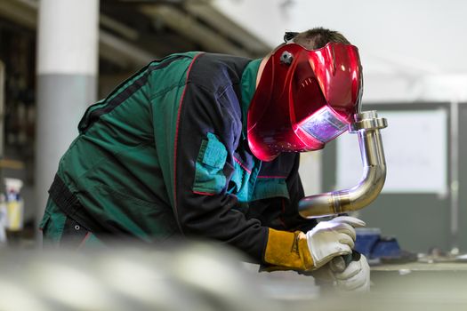 Industrial worker with protective mask welding inox elements in steel structures manufacture workshop.