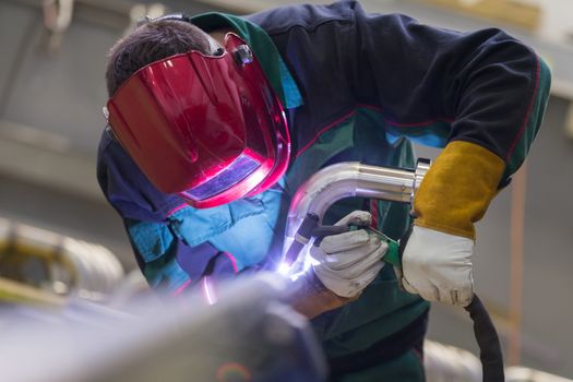 Industrial worker with protective mask welding inox elements in steel structures manufacture workshop.