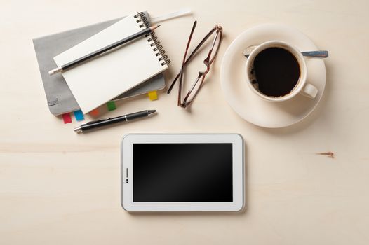 Small tablet pc, notebooks, pen, glasses, and coffee cup on wood table in cafe at morning time