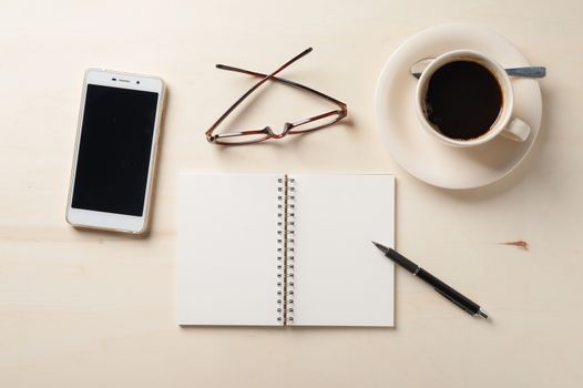 Opened notebook with blank area, pen, smart phone, and coffee cup on wood table in morning time