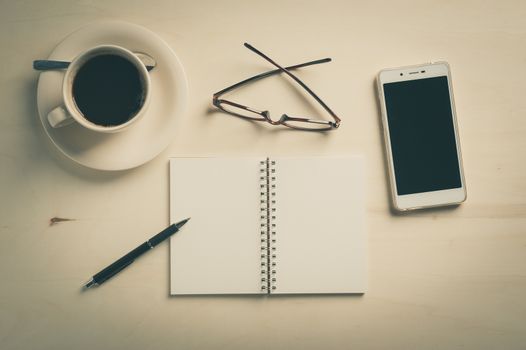 Opened notebook with blank area, pen, smart phone, and coffee cup on wood table in morning time with vintage filter effect