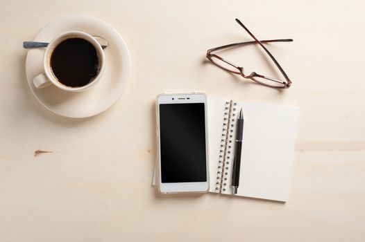 Opened notebook with blank area, pen, smart phone, and coffee cup on wood table in morning time